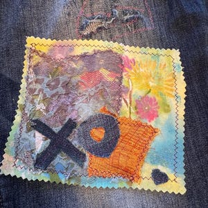 Peut inclure: Gros plan sur un tissu en jean avec un patch cousu coloré. Le patch présente un design "XO" avec un cœur, et diverses textures et couleurs de tissu, notamment orange, violet et bleu. Les bords du patch sont finis avec une couture en zigzag.