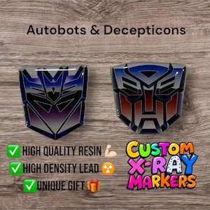 May include: Two Transformers logos, one blue and red and the other purple and silver, are displayed on a wooden surface. The logos are made of high-quality resin and are available as custom X-ray markers. The text "HIGH QUALITY RESIN", "HIGH DENSITY LEAD", and "UNIQUE GIFT" are displayed below the logos.