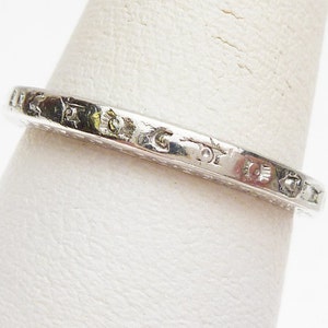 May include: A silver band ring with a decorative pattern and a small diamond on the side.