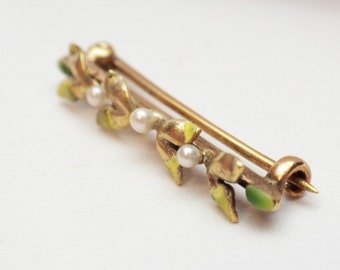 May include: A gold-toned brooch with a floral design. The brooch features three stylized flowers with green and yellow enamel and three white pearls.