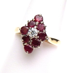 May include: A gold ring featuring a cluster of deep red rubies surrounding a central, sparkling diamond. The ring's design is a floral arrangement, with the gemstones set in a prong setting. The band is a simple, polished gold.