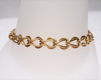 May include: A gold chain bracelet with a unique, intricate design. The links are oval-shaped and have a textured surface.