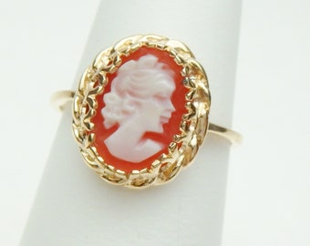 Op de afbeelding: Een gouden ring met een cameo van een vrouwenprofiel, gezet in een rode steen. De ring is omgeven door een gouden kettingontwerp.