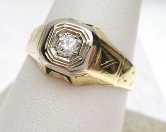 May include: A gold ring with a single diamond set in a white gold bezel. The ring has an intricate engraved design on the band.