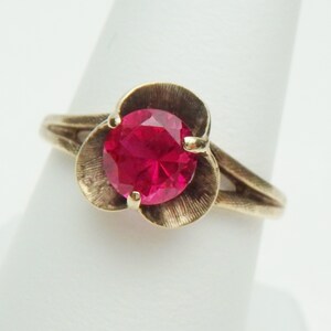 May include: A gold ring with a red gemstone set in a flower-shaped design.