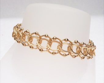 May include: A gold chain bracelet with a unique design featuring interlocking oval links and small round beads.