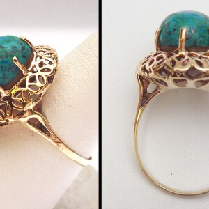 May include: A gold ring featuring a large, oval-shaped turquoise gemstone. The gemstone is held in place by prongs and surrounded by an ornate, openwork filigree design. The ring's band is a simple, polished gold.
