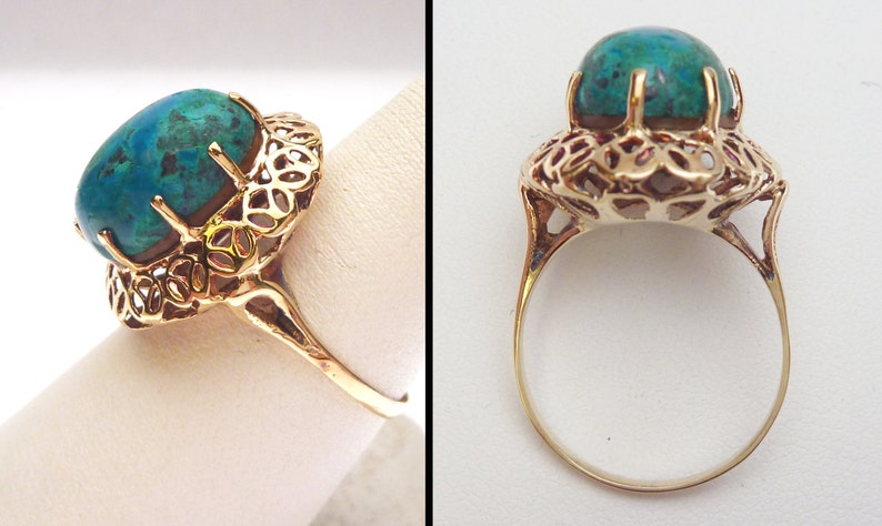 May include: A gold ring featuring a large, oval-shaped turquoise gemstone. The gemstone is held in place by prongs and surrounded by an ornate, openwork filigree design. The ring's band is a simple, polished gold.