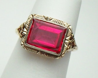 May include: A gold ring with a large, rectangular, red gemstone set in a filigree design.