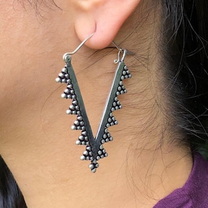 May include: Silver dangle earrings with a V-shaped design and a beaded edge.