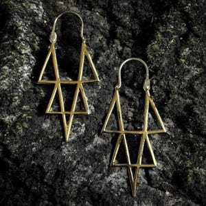 Könnte beinhalten: Ein Paar goldfarbene Ohrringe mit geometrischem Design. Jeder Ohrring hat eine Reihe von verbundenen Dreiecken, die eine einzigartige und moderne Ästhetik schaffen. Die Ohrringe werden vor einem dunklen, strukturierten Hintergrund präsentiert.