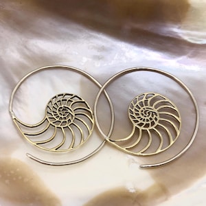 May include: A pair of gold-toned hoop earrings with a nautilus shell design. The earrings are delicate and intricate, with a spiral pattern that resembles a seashell.