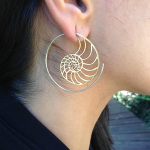 Puede incluir: Pendientes de aro dorados con un dise&ntilde;o de concha de nautilus. Los pendientes son grandes y tienen un dise&ntilde;o delicado e intrincado.