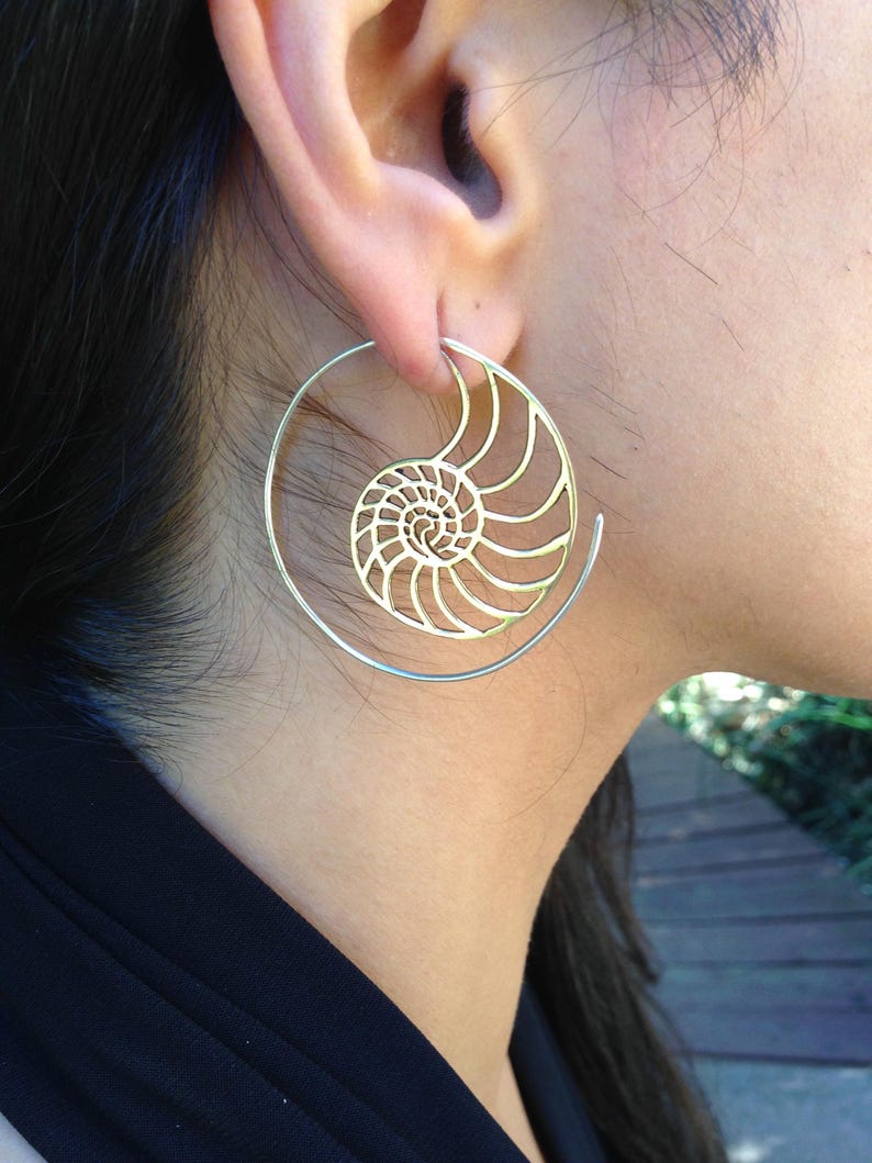 Puede incluir: Pendientes de aro dorados con un dise&ntilde;o de concha de nautilus. Los pendientes son grandes y tienen un dise&ntilde;o delicado e intrincado.