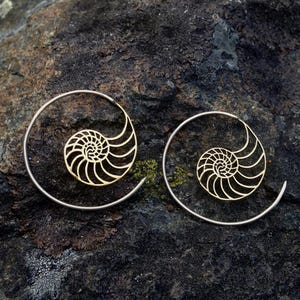 Puede incluir: Un par de pendientes de aro de plata con un dise&ntilde;o de concha de nautilus de oro. Los pendientes son delicados y femeninos.