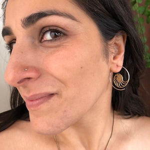 May include: A woman wearing a gold hoop earring with a nautilus shell design. The earring is in her right ear. She is also wearing a small gold nose ring.