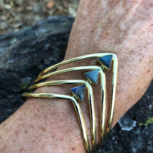 May include: Gold bangle bracelet with three triangular labradorite gemstones. The bracelet is layered and has a curved shape.
