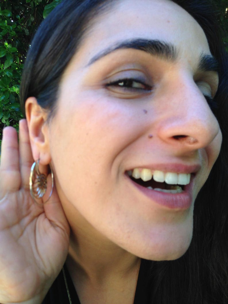 Puede incluir: Una mujer con cabello oscuro sonr&iacute;e y escucha atentamente. Lleva un aro de oro en la oreja izquierda.
