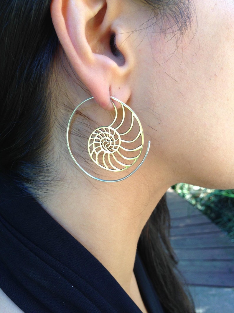 Puede incluir: Pendientes de aro dorados con un dise&ntilde;o de concha de nautilus. Los pendientes son grandes y tienen un dise&ntilde;o delicado e intrincado.