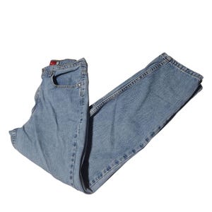 May include: Light blue denim jeans. The jeans are folded and have a classic five-pocket design. The denim has a faded appearance, and the stitching is visible. The jeans are made of a durable cotton blend.