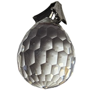 May include: A faceted crystal teardrop pendant with a dark metal clasp. The crystal is clear with a geometric pattern. The pendant is designed to catch and reflect light.