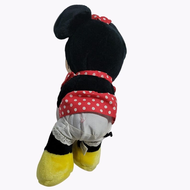 May include: A black and red plush toy of Minnie Mouse wearing a red and white polka dot dress and a white underskirt. The toy has yellow shoes and black eyes.