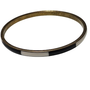 May include: A gold-toned bangle bracelet with black and white enamel inlays. The bracelet has a simple, circular design and is likely made of metal. The black and white sections are evenly spaced around the bracelet.