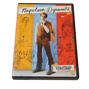 Puede incluir: DVD de la película "Napoleon Dynamite" con una portada colorida. La portada presenta un personaje con un traje marrón frente a taquillas. El texto incluye el título de la película y una cita: "YOU'LL LAUGH TILL IT HURTS...SWEET!"