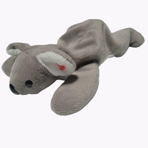 May include: A gray plush koala toy with a black nose, black eyes, and white ear accents. The koala has a red heart-shaped detail on one ear. The toy is lying down on a white background.