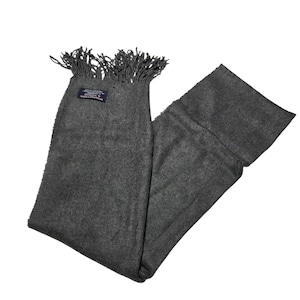 Pode incluir: Uma echarpe cinza carvão com bordas com franjas. A echarpe é feita de um material macio e tem formato retangular. Uma pequena etiqueta está presa perto da franja. A echarpe está dobrada e drapeada.