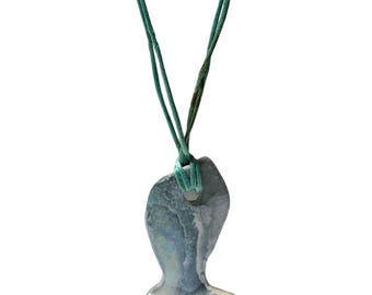 May include: A pendant shaped like a fish with a marbled blue, gray, and white finish. The pendant is suspended from a thin, teal-colored cord that passes through a hole at the top of the fish-shaped piece, creating a simple necklace design.