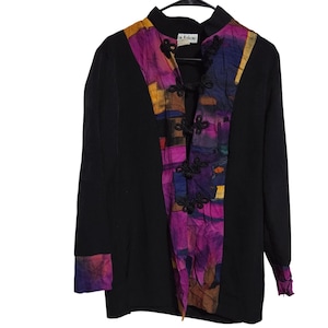 May include: Black long-sleeve jacket with a mandarin collar and decorative frog closures. The front panel features a colorful patchwork design in shades of purple, yellow, and blue. The cuffs also have a matching patchwork design.