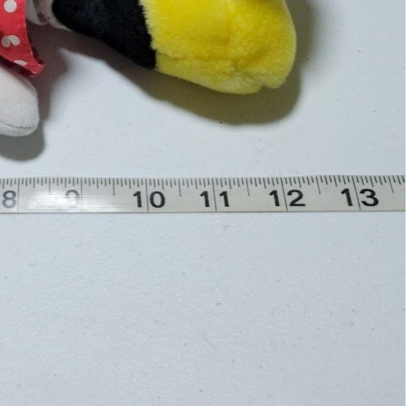 May include: A close-up of a white measuring tape with black markings. The numbers 8, 9, 10, 11, 12, and 13 are visible. The tape is lying flat on a white surface.