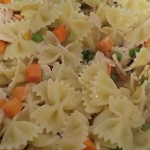 May include: Close-up of a pasta salad with farfalle pasta, diced carrots, green peas, and shredded chicken. The salad has a creamy, light-colored dressing. The ingredients are mixed together.