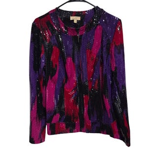 Op de afbeelding: Een jack met lange mouwen en ritssluiting met een levendig abstract patroon in magenta, paars en zwart. Het kledingstuk is volledig bedekt met kleine, reflecterende vierkante lovertjes en heeft een opstaande kraag en een centrale rits.