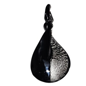 May include: A teardrop-shaped glass pendant with a twisted top. The pendant is divided into two sections: one half is solid black, and the other half features a silver, textured pattern. The glass has a glossy finish.