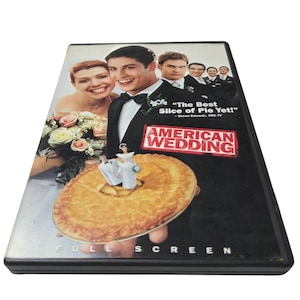 Peut inclure: Boîtier DVD du film "American Wedding". La couverture présente un thème de mariage avec une mariée et un marié, une tarte et le texte "The Best Slice of Pie Yet !" et "American Wedding".