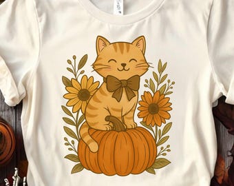 May include: Cream-colored t-shirt featuring a cartoon cat with a bow tie sitting on a pumpkin. The cat is orange with brown stripes. Yellow sunflowers and green leaves surround the cat and pumpkin design.