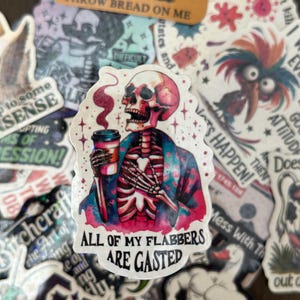 May include: A collection of stickers with various designs. The central sticker features a skeleton figure in a floral patterned jacket, holding a coffee cup, with the text "ALL OF MY FLABBERS ARE GASTED". Other stickers include text and illustrations.