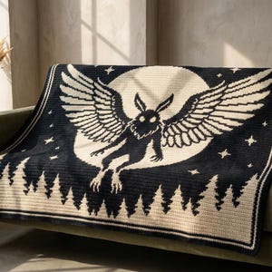 May include: A rectangular crochet blanket featuring a black and cream color scheme. The design displays a central winged creature silhouette against a large circular moon, surrounded by small stars above a forest of pine trees along the bottom edge.