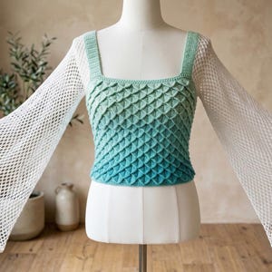 May include: A handmade, two-piece top on a mannequin. The top features a square neckline and a textured, ombre design that fades from green to blue. The sleeves are made of a white, open-weave fabric, creating a unique, airy look.