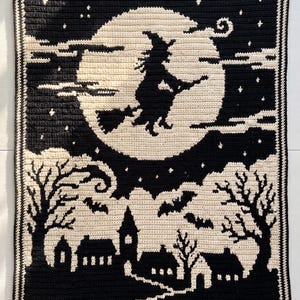 May include: A rectangular crochet blanket featuring a black and cream color scheme. The design depicts a silhouette of a witch flying on a broomstick in front of a large full moon, with a village, bare trees, and flying bats in the foreground.
