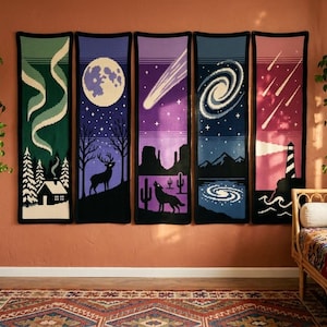 May include: Five vertical wall hangings featuring celestial and nature scenes. The panels depict an aurora borealis over a cabin, a deer under a full moon, a desert landscape with a howling wolf, a spiral galaxy over mountains, and a lighthouse.