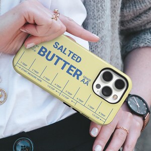Pu&ograve; includere: Custodia per telefono gialla con la scritta blu "SALTED BUTTER". Presenta una guida di misurazione con misure in cucchiai e tazze. La custodia &egrave; progettata per uno smartphone.