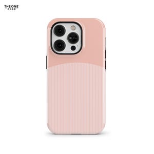 Puede incluir: Una funda para smartphone de color rosa claro con una sección superior lisa y una sección inferior con rayas verticales. El área del módulo de cámara está bordeada en negro, con tres lentes circulares y un flash. El texto THE ONE CASE es visible.