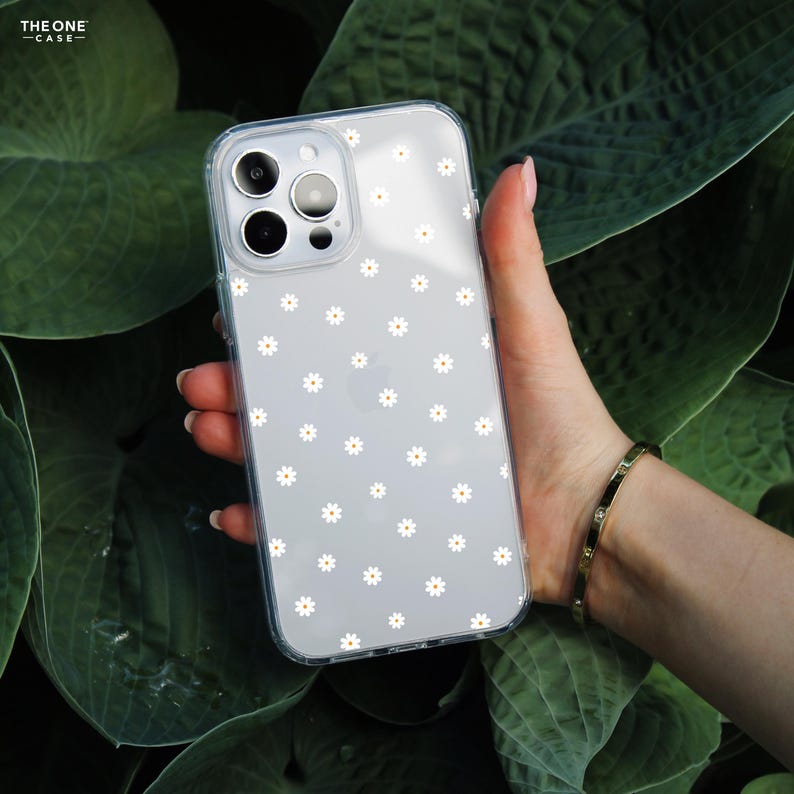 May include: A clear phone case with a white daisy pattern. The case is designed for an iPhone 14 Pro Max.