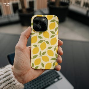 Op de afbeelding: Een telefoonhoesje met een citroenpatroon. De hoes heeft een cr&egrave;mekleurige achtergrond met gele citroenen en groene bladeren. De telefoonhoes wordt in een hand gehouden. De tekst "THE ONE CASE" staat in de linkerbovenhoek.
