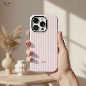 Pu&ograve; includere: Una custodia per telefono a righe rosa e bianche con le iniziali "ER" in basso al centro. La custodia del telefono ha una protezione per l'obiettivo della fotocamera nera. Il marchio "THE ONE CASE" si trova nell'angolo in alto a sinistra.