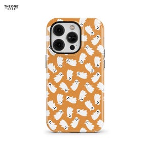 May include: A phone case with a repeating pattern of white cartoon ghosts on an orange background. The case has a camera cutout and the text "THE ONE -CASE-" in the upper left corner.