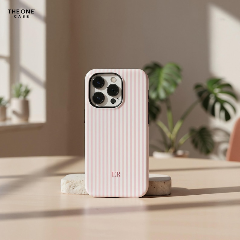 Pu&ograve; includere: Custodia per telefono a righe rosa e bianche con le iniziali "ER". La custodia &egrave; su una piccola pietra. Il marchio "THE ONE CASE" si trova nell'angolo in alto a sinistra. La custodia ha un ritaglio per la fotocamera.